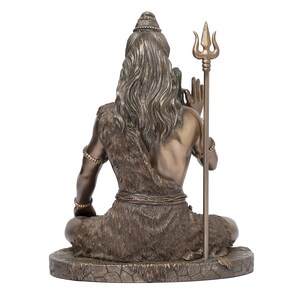 Puede incluir: Estatua de bronce de una figura sentada con pelo largo y una prenda similar a piel. La figura sostiene un tridente y lleva pulseras de cuentas. La estatua est&aacute; sobre una base texturizada, mostrando detalles intrincados.