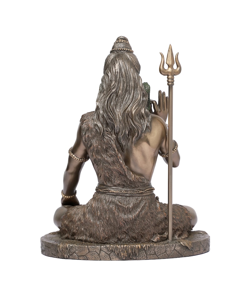 Puede incluir: Estatua de bronce de una figura sentada con pelo largo y una prenda similar a piel. La figura sostiene un tridente y lleva pulseras de cuentas. La estatua est&aacute; sobre una base texturizada, mostrando detalles intrincados.