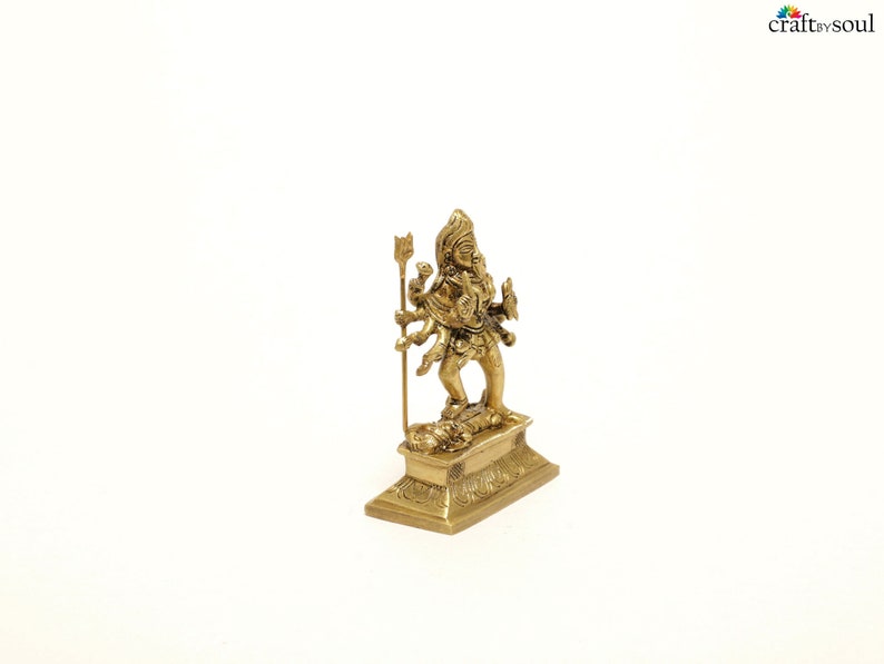 Puede incluir: Una peque&ntilde;a y detallada estatua de lat&oacute;n de una deidad de m&uacute;ltiples brazos, de pie sobre una base rectangular. La figura sostiene un tridente y otros objetos simb&oacute;licos. La estatua tiene intrincadas tallas y est&aacute; sobre un fondo blanco.