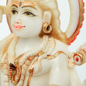 May include: A detailed, close-up of a white marble statue of a deity with intricate gold and red accents. The statue features detailed facial features, jewelry, and a halo. The overall theme is religious art.