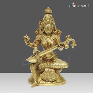 Puede incluir: Estatua de lat&oacute;n dorado de una deidad sentada tocando un instrumento de cuerda. La estatua presenta detalles intrincados en la ropa, las joyas y los rasgos faciales. La base es redonda y decorada. El logotipo "craft by soul" est&aacute; en la esquina superior derecha.