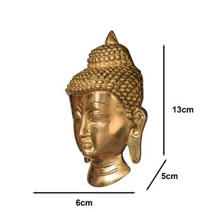 Puede incluir: Una escultura de cabeza de Buda dorada. La escultura mide 13 cm de alto, 6 cm de ancho y 5 cm de profundidad. La cabeza presenta rasgos faciales detallados y una toca texturizada. El producto es de craftbysoul.