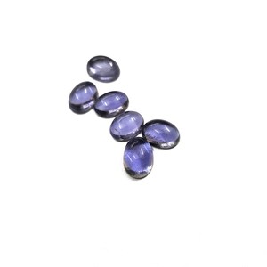 Puede incluir: Seis piedras preciosas ovaladas y translúcidas en varios tonos de púrpura están dispersas sobre una superficie blanca. Las gemas tienen un aspecto liso y pulido, reflejando la luz. Las piedras preciosas son probablemente para la fabricación de joyas.