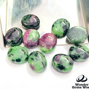 Puede incluir: Una colección de diez piedras preciosas ovaladas de color verde, negro y rosa. Las piedras preciosas son lisas y pulidas.