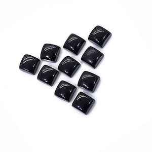 May include: Twelve black square-shaped cabochons, likely gemstones, arranged in a pattern on a white background.
