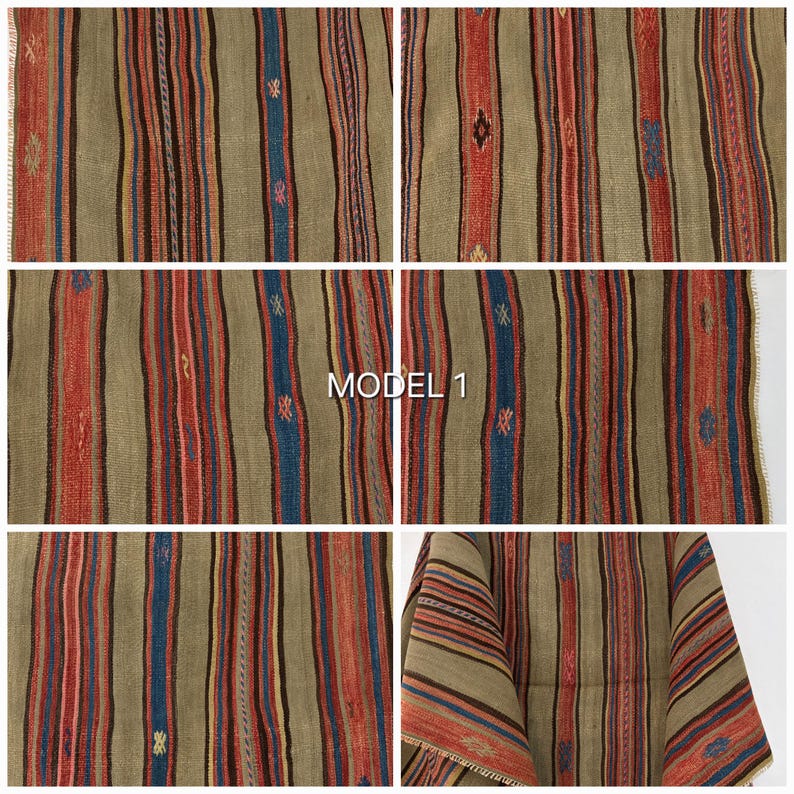 Op de afbeelding: Een geweven textielstof met een herhalend patroon van verticale strepen in olijfgroen, rood, donkerbruin en blauw. De stof vertoont kleine, verspreide geometrische motieven in geel, roze en blauw. De tekst MODEL 1 is zichtbaar.