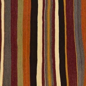 May include: A woven textile featuring a repeating vertical striped pattern in shades of deep burgundy, burnt orange, mustard yellow, charcoal gray, black, and off-white. The fabric displays a textured weave with small geometric accents.