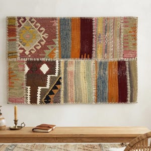 May include: A rectangular wall hanging composed of multiple stitched fabric panels featuring diverse patterns and colours including deep red, orange, blue, brown, and cream. The textile sections are joined by visible white whipstitch detailing.