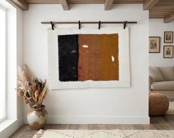 May include: A rectangular wall hanging featuring a central panel with three vertical color blocks in black, rust, and mustard yellow. The panel is stitched onto a larger off-white fabric backing and suspended from a dark wooden rod.