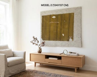 May include: A rectangular wall hanging titled MODEL 2 (134X107 CM) featuring a large olive green central panel with white stitched details and small white shapes, bordered by a textured light gray fabric frame, mounted on a plain white wall.