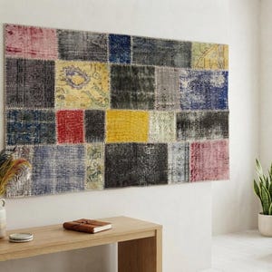 Peut inclure: Une grande tapisserie murale rectangulaire présentant un motif en patchwork composé de divers segments de tissu dans des tons de rose, jaune, bleu, rouge, gris et noir, avec des coutures visibles reliant chaque pièce rectangulaire.