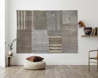 May include: A large rectangular wall tapestry composed of multiple stitched fabric panels in varying shades of gray, brown, and beige. The textile features a mix of solid, striped, and textured sections, creating a patchwork appearance on the wall.