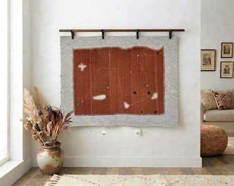 May include: A rectangular wall hanging featuring a rust-colored center panel with white embroidered constellation patterns, bordered by a light gray textured fabric. The piece is suspended from a dark wooden rod with four black metal brackets.
