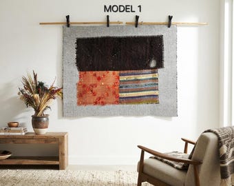 May include: A rectangular wall hanging featuring a light grey base fabric with three stitched-on patches: a large dark brown section, an orange floral patterned section, and a multi-coloured striped section. The text MODEL 1 appears above.