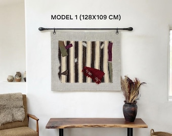 May include: A rectangular wall hanging featuring a striped brown and cream fabric panel with attached patches in olive, purple, and red. The piece is suspended from a black metal rod and measures 128x109 cm as indicated by the text MODEL 1.