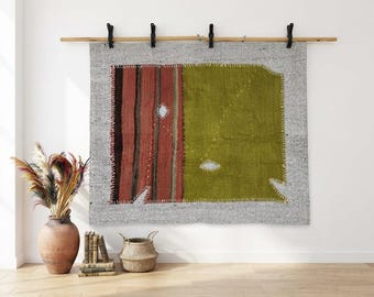 May include: A rectangular wall hanging featuring a gray textured background with a central panel of vertical red and brown stripes next to a solid olive green section. The piece is finished with visible white whip-stitching along the edges.