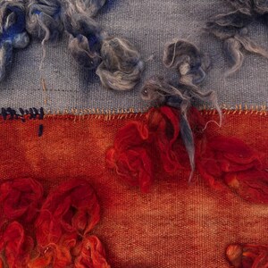 May include: Close-up of a textile artwork featuring a blend of textures and colors. The upper section displays a light blue fabric with tufts of gray and blue fibers. The lower section showcases a vibrant orange-red hue with similar fiber accents.