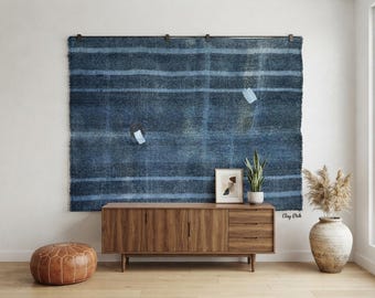 May include: A large rectangular wall hanging featuring horizontal stripes in varying shades of dark blue and light blue. The textile has a textured appearance with frayed edges and is suspended from a dark metal rod with four visible mounting clips.