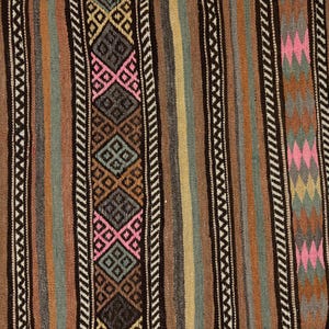 Op de afbeelding: Een geweven textielkleed met verticale strepen in tinten bruin, beige, grijs en gedempt groen. Het ontwerp bevat herhalende geometrische ruitpatronen in roze, donkergrijs en bruin, geaccentueerd door smalle zwart-witte zigzagranden.