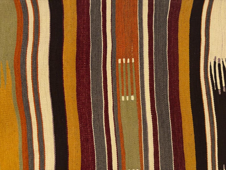 May include: A woven textile featuring a repeating pattern of vertical stripes in shades of mustard yellow, deep burgundy, charcoal gray, cream, and sage green. The fabric displays a textured, flat-weave construction with subtle variations in color.