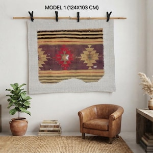 May include: A rectangular woven textile wall hanging featuring a geometric pattern in shades of red, brown, and tan, suspended from a wooden rod by four black clips. The textile is labeled MODEL 1 (124X103 CM) and displays a central diamond motif.