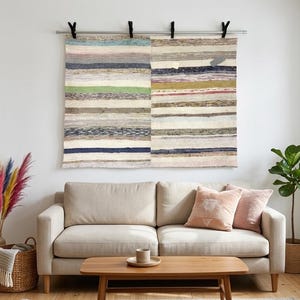 May include: A rectangular woven wall hanging featuring horizontal stripes in various colours including blue, green, pink, and cream. The textile is suspended from a silver metal rod using four black clips, displaying a textured, multi-coloured pattern.