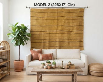 Könnte beinhalten: Ein großer senfgelber Wandbehang mit dünnen horizontalen dunkelbraunen Streifen, der an einer Metallstange hängt. Das Textil zeigt oben den Text "MODEL 2 (226X171 CM)", der die Abmessungen in Zentimetern angibt.