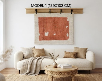 Puede incluir: Un tapiz rectangular titulado MODEL 1 que mide 129x102 cm, con un gran parche rectangular de color terracota centrado sobre una base de tela color crema, suspendido de una barra de madera con cuatro clips negros.