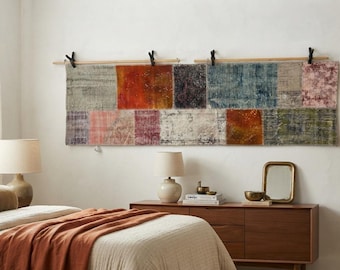 May include: A rectangular wall hanging composed of multiple stitched fabric panels in varied colors including orange, blue, pink, and grey. The textile is suspended from two horizontal wooden rods by four black clips attached to the wall.