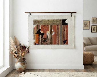 May include: A rectangular textile wall hanging featuring a patchwork of various woven fabrics in shades of rust, orange, brown, and cream. The piece is suspended from a dark wooden rod and displays visible stitching along the edges of the fabric panels.