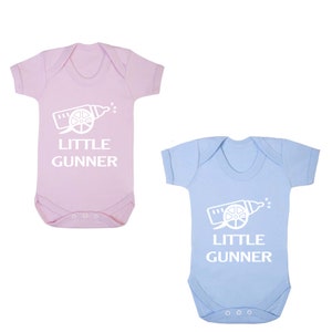 May include: Two baby onesies, one pink and one blue, with a white graphic of a baby bottle shaped like a cannon and the text "LITTLE GUNNER".