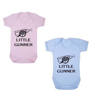 May include: Two baby vests, one pink and one light blue, with a black graphic of a baby bottle shaped like a cannon with the text "LITTLE GUNNER" underneath.