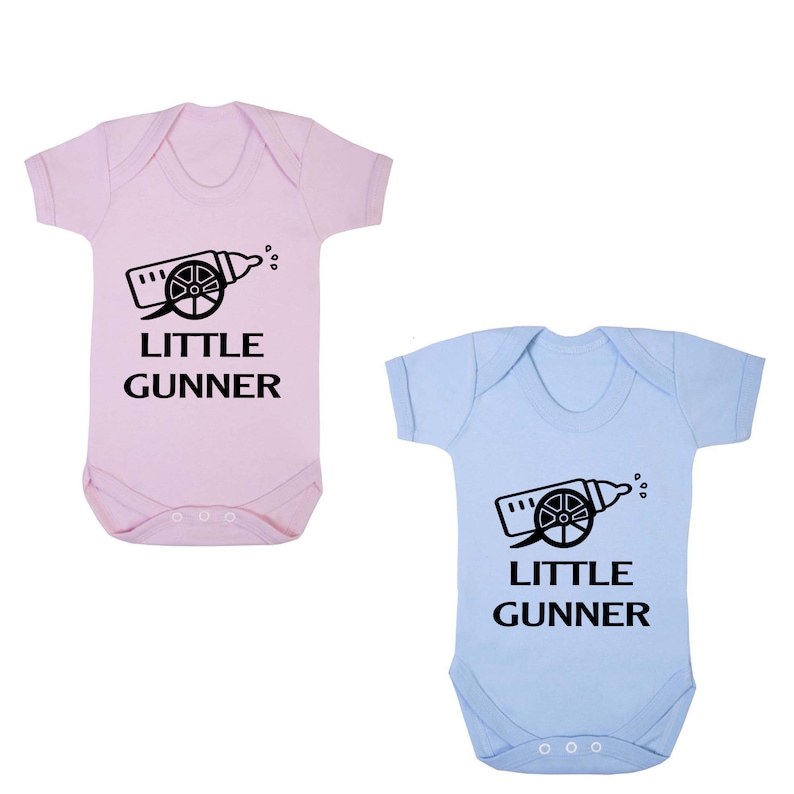 May include: Two baby vests, one pink and one light blue, with a black graphic of a baby bottle shaped like a cannon with the text "LITTLE GUNNER" underneath.