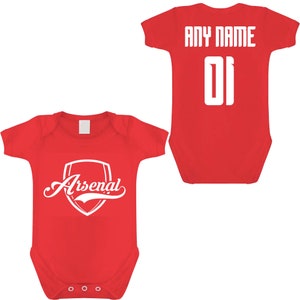 May include: Red baby bodysuit with the Arsenal logo in white on the front. The back of the bodysuit has the text "ANY NAME" above the number "01" in white. The bodysuit is designed for infants.