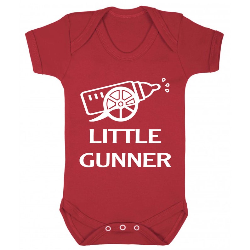 May include: Red babygrow with a white graphic of a baby bottle shaped like a cannon with the text "LITTLE GUNNER".