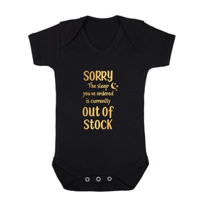 May include: Black baby growsuit with gold text that reads "SORRY The sleep you've ordered is currently OUT OF STOCK".