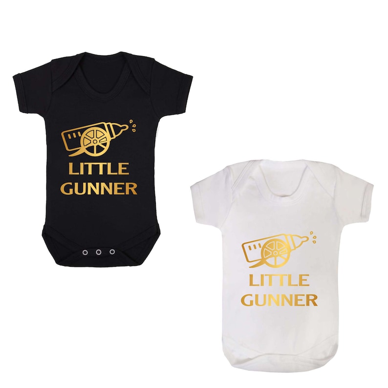 May include: Two baby onesies, one black and one white, with a gold graphic of a baby bottle shaped like a cannon and the text "Little Gunner".