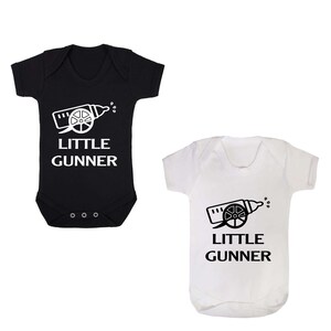 May include: Two baby onesies, one black and one white, with a white graphic of a baby bottle shaped like a cannon with the text "Little Gunner" underneath.