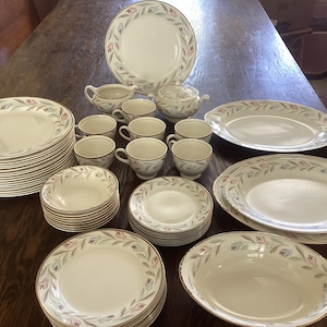 May include: A set of white dinnerware with a floral pattern in shades of pink, green, and brown. The set includes plates, bowls, and cups.