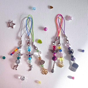 May include: Five colourful beaded phone charms with different metal charms, including a star, a music note, a crescent moon, a flower, and a microphone.