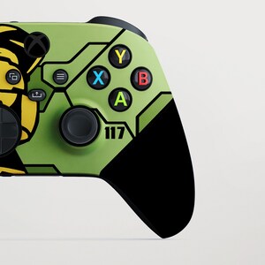 May include: A custom video game controller in green and black. The controller has a unique design with the number "117" and coloured buttons: Y (yellow), X (blue), B (red), and A (green). The controller has a black D-pad and analogue sticks.
