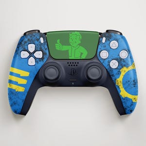 May include: A custom blue and black video game controller with a Fallout theme. The controller features a green screen with a Vault Boy graphic, blue accents, and yellow gear and stripe designs.