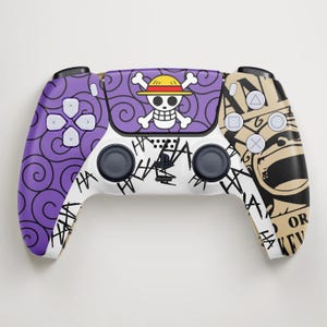 May include: A custom PlayStation 5 controller with a One Piece theme. The controller has a purple and white design with a skull and crossbones, and the word "HA" in a graffiti style.