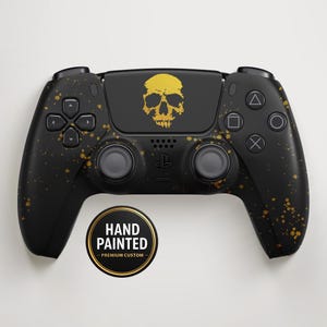 Peut inclure: Manette de jeu noire peinte à la main avec des éclaboussures dorées et un motif de crâne doré. La manette porte un autocollant circulaire indiquant "HAND PAINTED - PREMIUM CUSTOM".