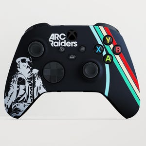 Può includere: Un controller per videogiochi wireless nero con il testo bianco ARC Raiders, una silhouette bianca di un personaggio e strisce diagonali in azzurro, crema e rosso. Il controller include pulsanti standard, joystick e un D-pad.