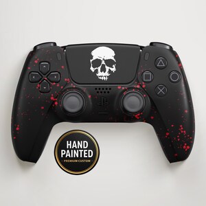 Könnte beinhalten: Schwarz handbemalter Videospiel-Controller mit weißer Totenkopf-Grafik und rotem Spritzdesign. Der Controller hat einen runden Aufkleber mit der Aufschrift "HAND PAINTED - PREMIUM CUSTOM".