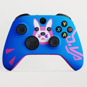 Può includere: Un controller per videogiochi wireless blu con una grafica di un coniglio rosa e bianco al centro. Il controller include levette analogiche nere, un pad direzionale nero e quattro pulsanti azione colorati etichettati Y, X, B e A. Accenti geometrici rosa sono visibili sui lati.