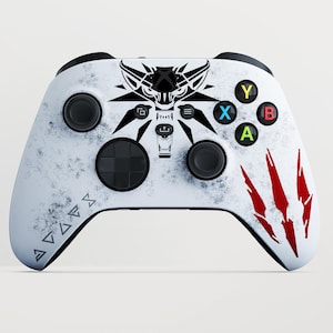 May include: A white video game controller featuring a distressed texture, a black wolf head graphic in the center, and three red claw marks on the right side. The left side displays a series of geometric symbols, and the buttons are colored.