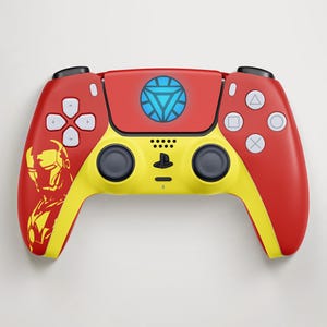 Może przedstawiać: Czerwono-żółty kontroler PlayStation 5 z motywem Iron Mana. Kontroler posiada symbol reaktora łukowego Iron Mana i sylwetkę Iron Mana. Przyciski są białe, a drążki czarne.