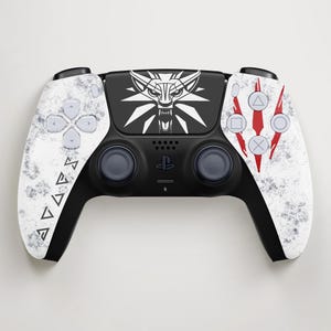 Könnte beinhalten: Ein schwarz-weißer kabelloser Gamecontroller mit einem Wolfskopf-Emblem auf dem zentralen Touchpad, einer verwitterten Steinstruktur an den Griffen, geometrischen Symbolen auf der linken Seite und drei roten Kratzspuren hinter den Aktionstasten.